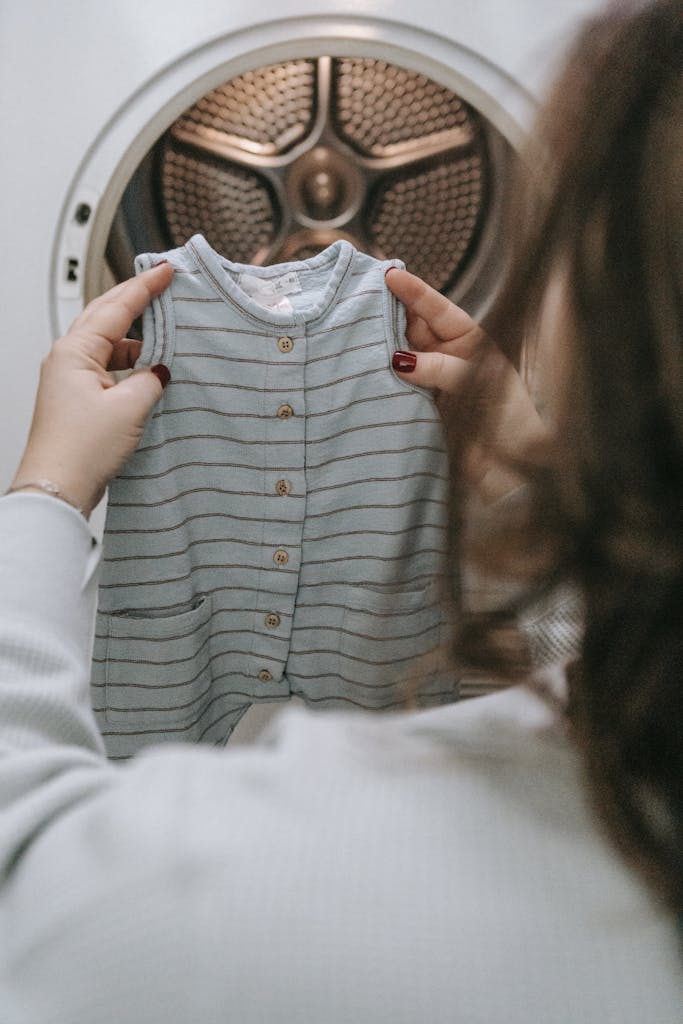 A woman holding a striped baby garment in front of a washing machine indoors.